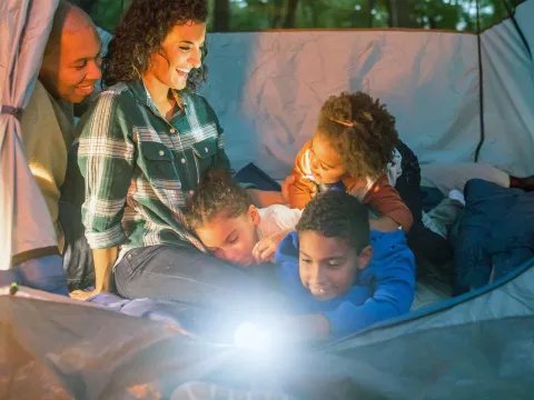 A family of five is snuggled together in a tent with a flashlight on.