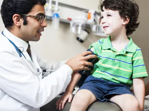 A child, sitting on an exam table, as a doctor takes his blood pressure.