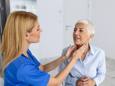 Doctor feeling the neck of a woman to check her thyroid.