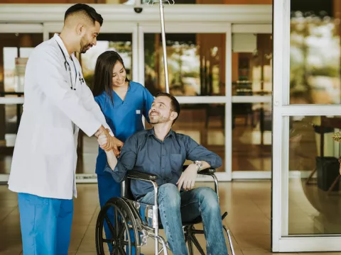 Doctor shaking hands with man as he leaves hospital in a wheelchair