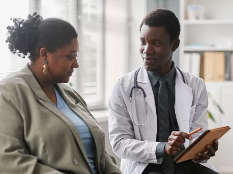A black woman patient talks with a black male doctor.