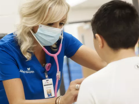 An AdventHealth employee using a stethoscope on a young teenager