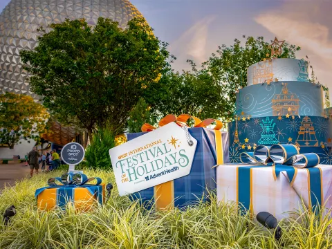 Epcot International Festival of the Holidays sign and presents with Spaceship Earth in the background.