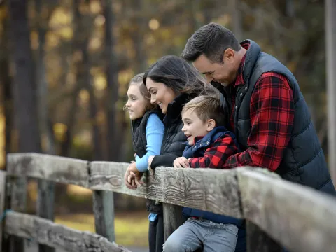 A family of four leaning on a fence while outdoors in the winter.
