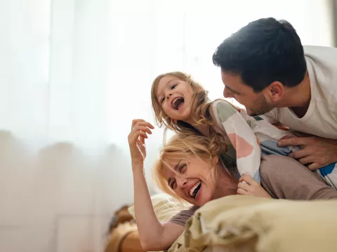 A family laughing while laying on a bed at home.