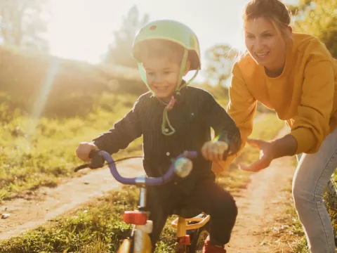A mom pushes her son a bike, outside.