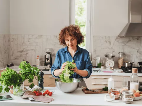 A woman making a bowl of salad in the kitchen. 