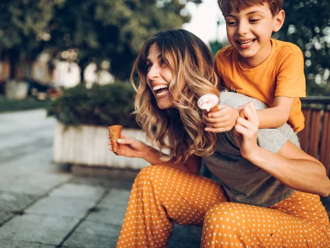 A Mother and Son Laugh and Play as They Eat Ice Cream Cones on a City Park Bench