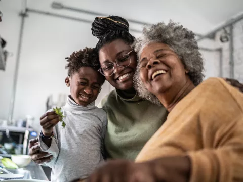 Grandmother, mother, and son smiling together while in the kitchen at home.