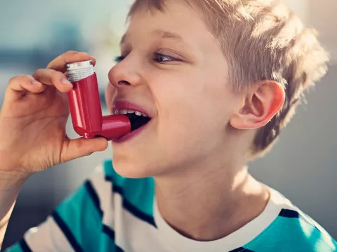 Young boy smiling about to take a puff from an inhaler.