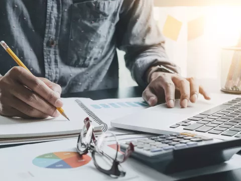 A gentleman working on his desk with his laptop, notebook, and calculator