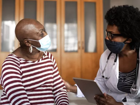 A doctor and patient discuss health care while wearing masks.