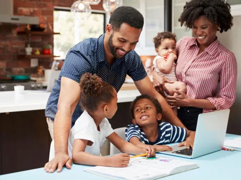 Photo of a family standing at a laptop making plans and smiling.