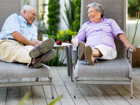 A couple chatting and laughing in lounge chairs outdoors.