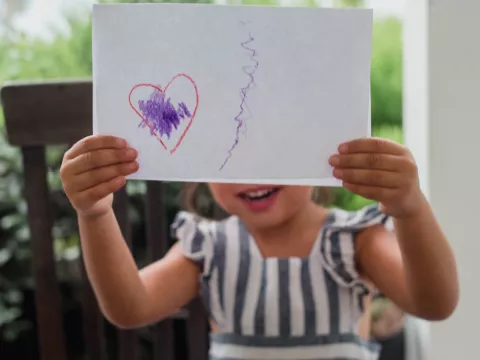 A little girl proudly displays her artwork for the camera.