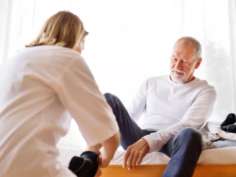 A senior gentleman being assisted in putting his socks on.