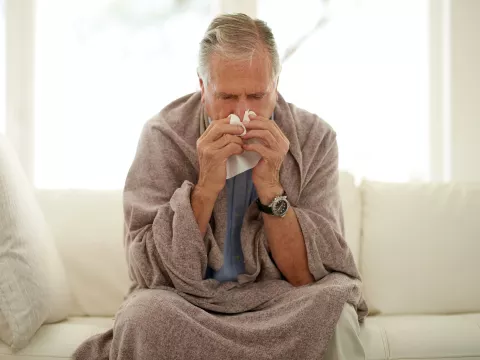 A man sneezing while at home on his couch. 