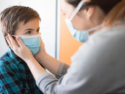 A mom puts a facemask on her son. 