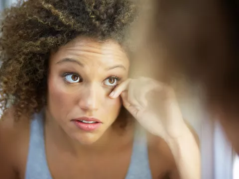 A woman examines her eye in a mirror.