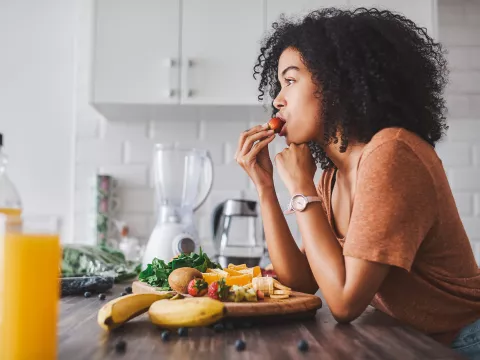 A woman eating a plate of fruit in her kitchen