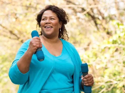 A woman exercising outdoors with hand weights. 