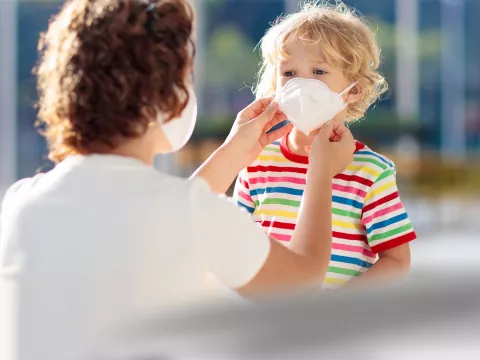 A mom helps her son position his face mask.