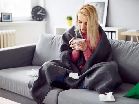 A woman drinking tea under a blanket at home. 