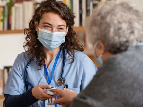 Hospice worker with mask talking to elderly patient 