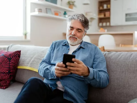 Older man looking at his phone while sitting on a couch.