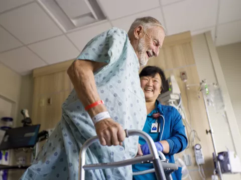 Older man using a walker with the help of a nurse