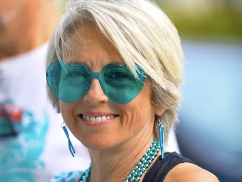 Anita Robinson, a woman with short blonde hair and tan skin, wearing teal heart-shaped sunglasses