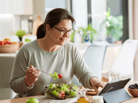 A woman eating a health meal while reading on a tablet.