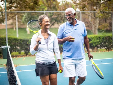 Two adults, walking off of the tennis court, talking to each other and having a great time.