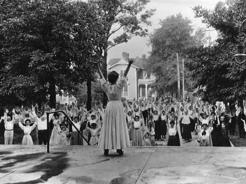 A woman leading out a group of people in breathing exercises while outdoors.