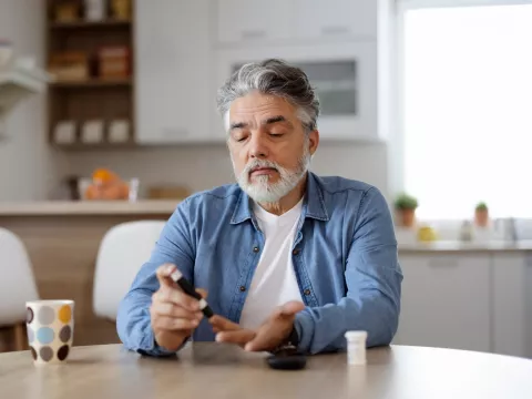 Man sitting in a kitchen using a glucose monitor.