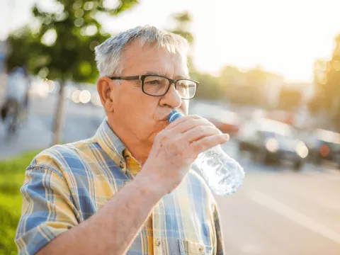 Older man drinking from a plastic water bottle.