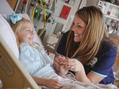 A female nurse consoles a young female patient in her hospital bed.
