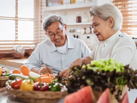 Senior couple sitting at the kitchen counter with produce on the kitchen table.