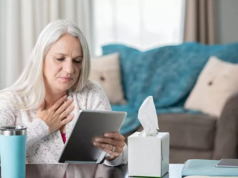 Woman holding heart, looking at tablet