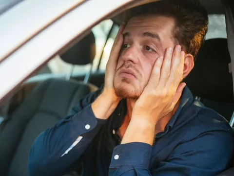 An upset man holds his face with his hands while sitting in a car.
