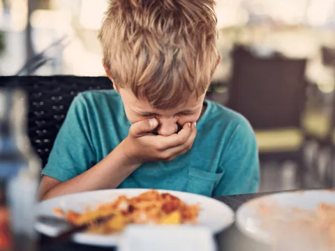 A young boy holding his hand over his mouth.