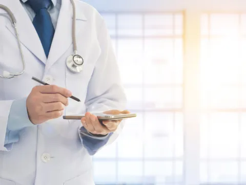 Physician holding a device and writing utensil in his hand
