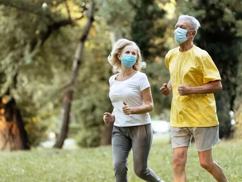 Older couple running outdoors while wearing masks.
