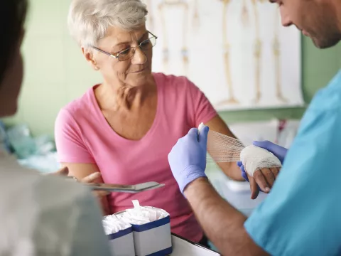 An older woman has her hand bandaged by a nurse