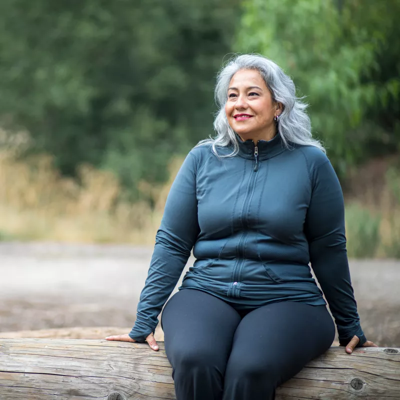 A Hispanic Woman Sits on a Log, Taking a Break From a Hike