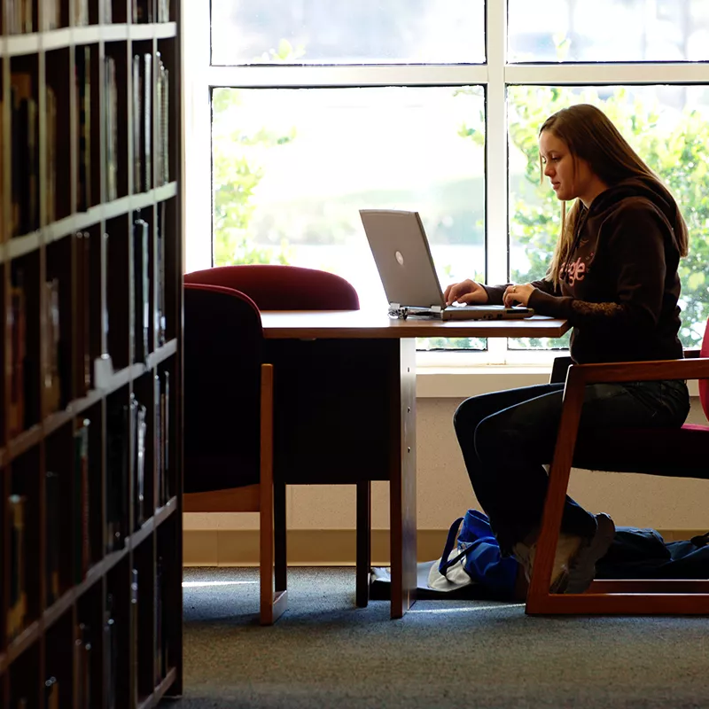 A girl sitting at a table in the library on her laptop.