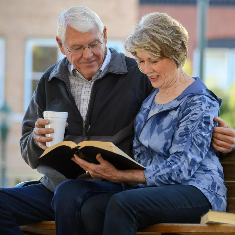 Elderly Couple sitting on a park bench reading the Bible.