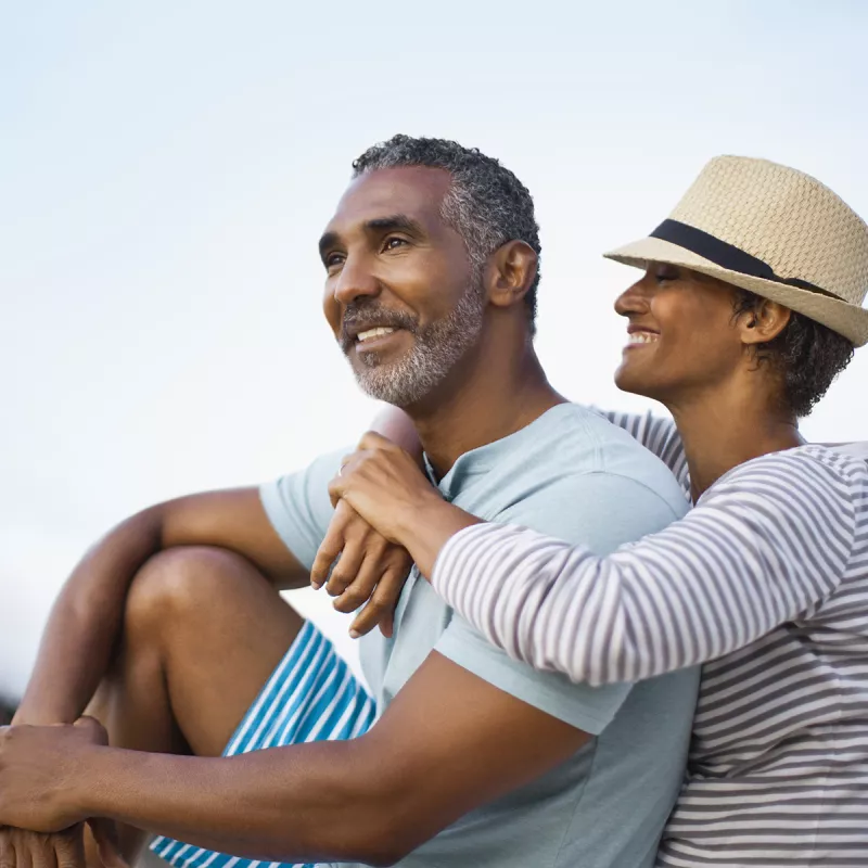 A smiling woman wraps her arms around her husband outdoors