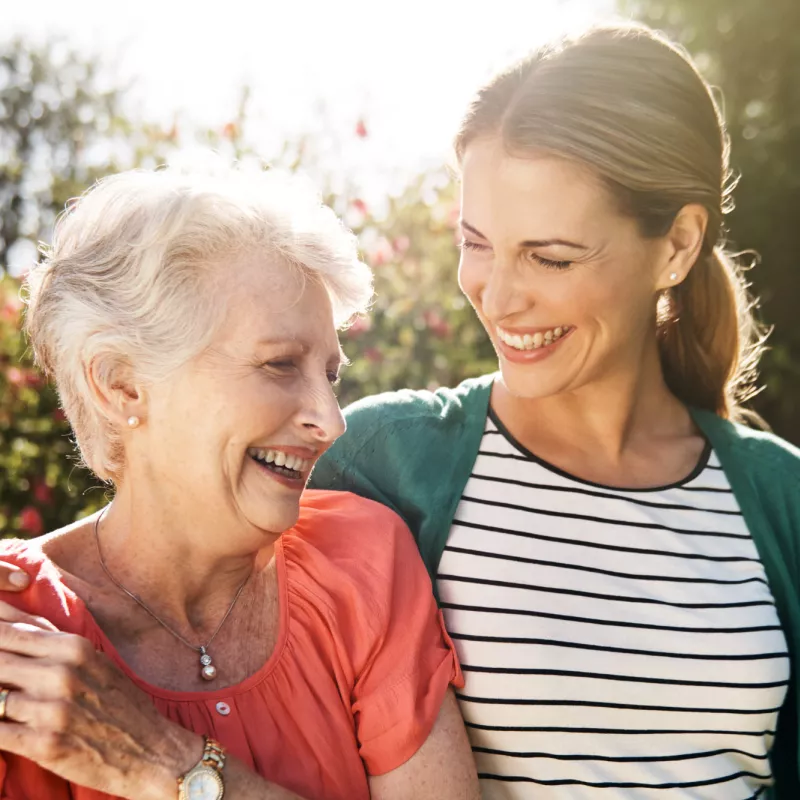 A senior woman with her adult daughter walking together outdoors.