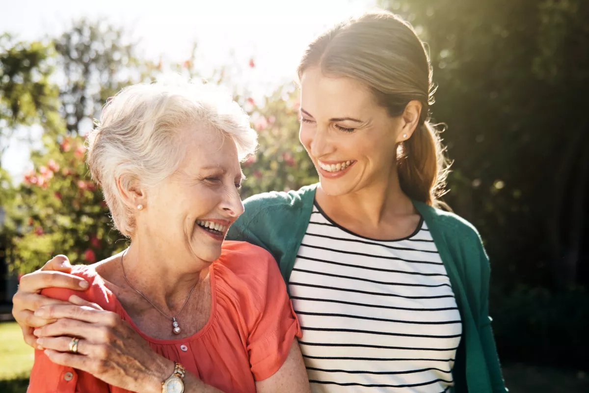 A senior woman with her adult daughter walking together outdoors.